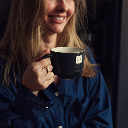 Person holding a mug with a visible brand label, wearing a blue shirt.